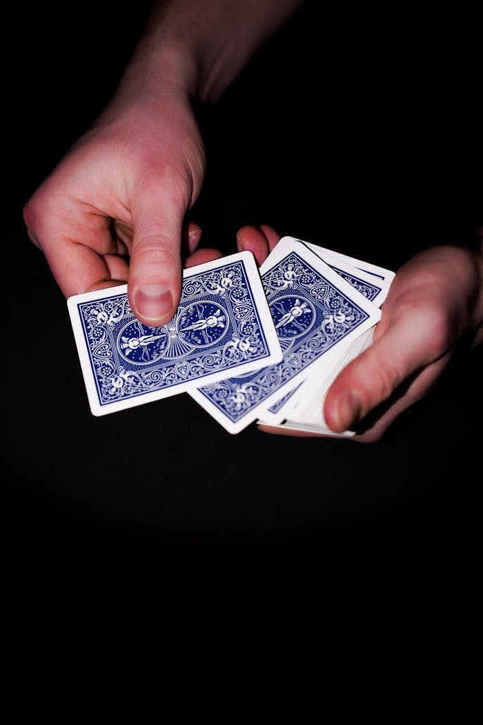 Hands shuffling blue playing cards against a dark background.